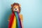 Young woman in lion mask with rainbow pride lgbt flag in mouth looking confused or overhelmed