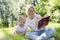 A young woman with a little daughter lie in the park on the grass and read a book. Pretty blonde with freckles on her face.