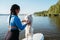 Young Woman with Locs Holding Her Pet Japanese Spitz on the Lake, Dog Standing on the Sup Board on His Back Paws