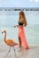 Young Woman with Long Blond Hair in Black Bikini and Pink Wrap Feeding Pink Flamingos on the Beach #3