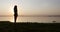 Young woman with long curly red hair standing on shore of the lake at the sunset.