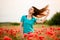 Young woman with long flowing hair standing on field with red poppies.