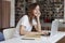 Young woman long hair analyst working at co-working office on laptop, look to camera, calm face, bookshelf behind, library