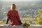 Young woman with long hair sits on a hill overlooking the city