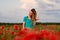 Young woman with long hair standing on field with red poppies.