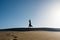 Young woman with long skirt dancing in the distance in evocative and confident way on top of desert dune with clear blue sky