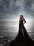 Young woman in long transparent black dress among beach and sea. Wind blows hem of her dress