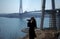 Young woman looking through binoculars on background of construction of cable-stayed bridge