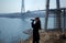 Young woman looking through binoculars on background of construction of cable-stayed bridge