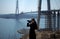 Young woman looking through binoculars on background of construction of cable-stayed bridge