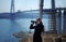 Young woman looking through binoculars on background of construction of cable-stayed bridge