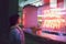 Young woman looking through the glass next to a club with a window with neon lights take away