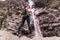 Young woman looking at splashing waterfall in rocky mountain. Caucasian Traveler standing before water stream