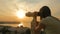 Young woman looking through tourist telescope, exploring city at sunset