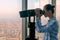 Young woman looking through tourist telescope and exploring cityscape