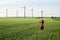 Young woman looking towards wind turbines at sunrise, in a field of green wheat. Concept for sustainable energy solutions.