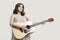 Young woman looking up while playing guitar against gray background