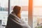 Young woman looking through the window at home wrapped in warm comfy blanket