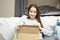 A young woman looks into the box, sitting at home on the couch, opens the parcel, smiles