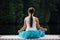 Young woman in the lotus position is practicing yoga in the forest next to the river. sitting on mats the wooden pier.