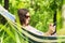 Young woman lying in a hammock in garden with E-Book.