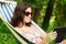 Young woman lying in a hammock in garden with E-Book.