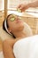 Young woman lying on massage table with cucumber slice being placed over eye