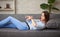 Young woman is lying at a sofa looking on her watch with shock