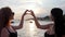 Young woman make heart hands on background sea, weekend outdoors, best girlfriends posing for photo at sunset,