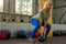 Young woman makes a cravings holding a weight with a green handle on the background of the composition of sports equipment