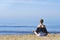 Young woman makes meditation in lotus pose on sea / ocean beach, harmony and contemplation. Beautiful girl practicing yoga at sea