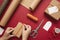 Young woman making bow on kraft gift boxe with orange thread on a red background.