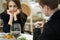 Young woman making an exasperated expression gesture on a bad date at the restaurant. Man looks at his watch.