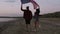 Young woman and man running on the sand with raised american flag, feeling freedom. Evening dusk. Tracking footage