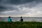 Young woman and man sitting in the field in front of a lake on an afternoon storm