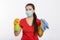 Young woman in mask and gloves holds spray bottle and rag isolated on a white background.