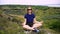 Young woman mediating in casual clothes sitting on a rock in nature among greenery