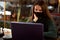 Young woman in medical mask in cafe with laptop