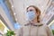 A young woman in a medical mask on a city street with shops