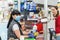 A young woman in a medical mask and gloves, working at the checkout in a supermarket. In the background, the buyer is blurred.