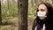 Young woman in medical mask on her face walking in forest on fresh air. Adult female covered her face with mask to