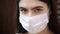 Young woman in medical mask looks into the camera; protection against coronavirus COVID-19