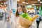 Young woman in a medical mask looks shocked at a paper check in a grocery supermarket holding a paper bag with groceries