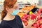 A young woman in a medical mask between rows of vegetables in a supermarket. Girl chooses bell pepper in the store. Flu virus