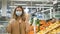 A young woman in a medical mask and rubber gloves selects fresh lemons in a grocery supermarket, looks at the camera