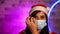 Young woman in medical mask and Santa Claus hat against illuminated wall. Close up of brunette in Christmas hat and