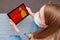 A young woman in a medical mask sits at home in quarantine and calls an online doctor for advice on the symptoms of coronavirus