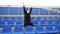 Young woman in medical mask sitting on stadium bleachers alone and rooting for her favorite sports team. Adult female