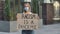 Young woman in medical mask stands with a cardboard poster RACISM IS A PANDEMIC in a public place outdoor. No racism