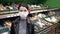 Young woman in medical mask stands in supermarket. Protection from coronavirus, purchase of food for quarantine. Defecit of